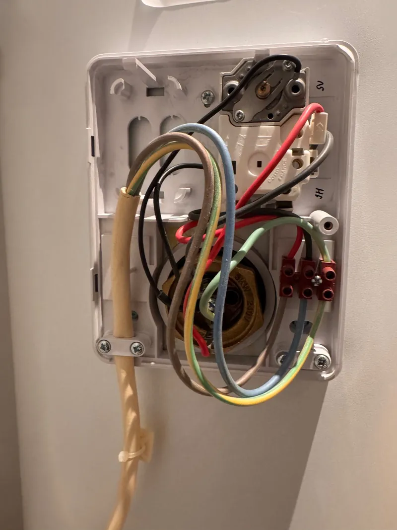 Immersion heater thermostat and wiring exposed behind the cover on the side of a hot water cylinder