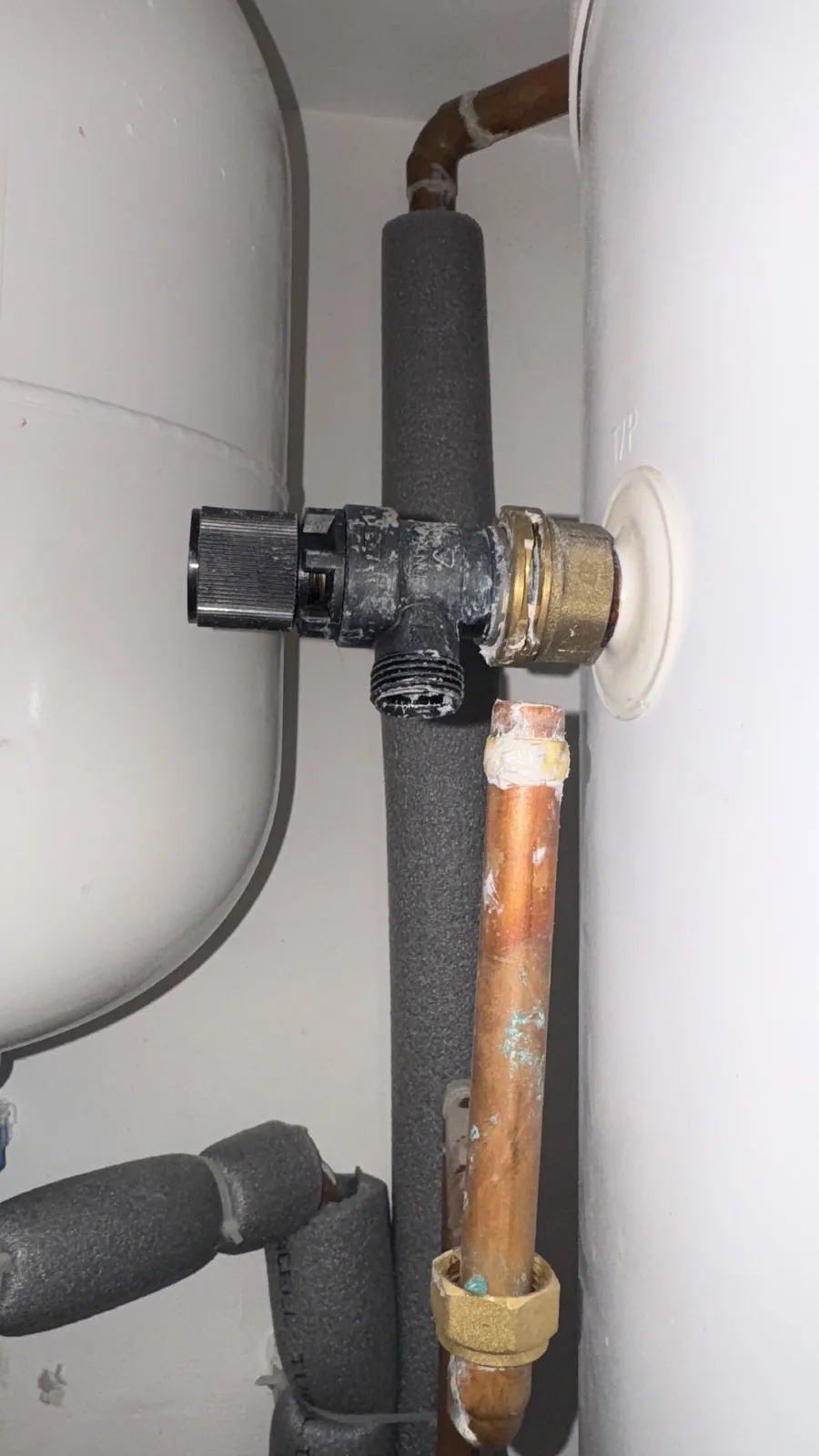 Black-bodied relief valve fitted to the side of an unvented cylinder beside the expansion vessel