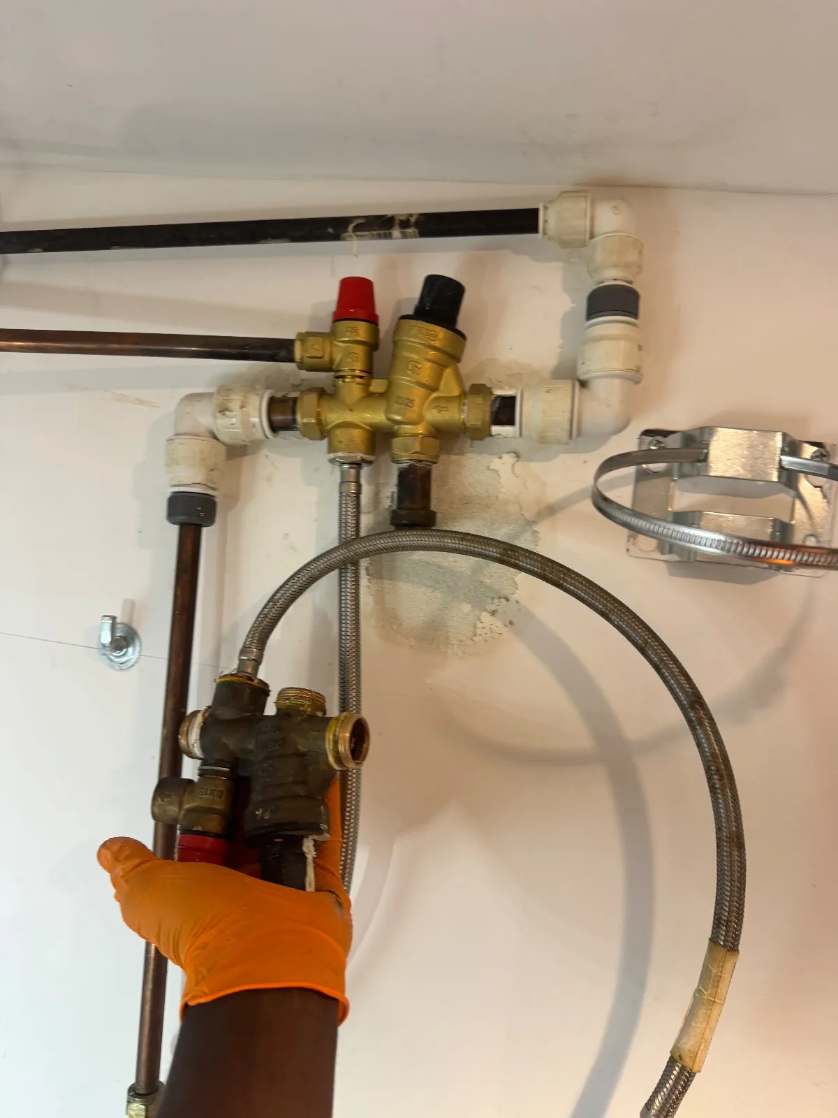 Gloved hand holding an old brass combination valve beside the new valve group fitted on the wall